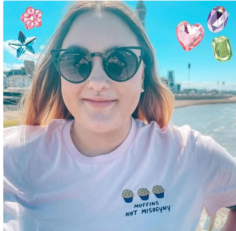 Woman by the sea wearing a pink Muffins Not Misogyny embroidered tee